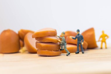 Minyatür insanlar: Kapatılan işçiler beyaz arka planda izole edilmiş sosisler üzerinde çalışıyorlar (gıda kavramı)