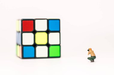 Minyatür insanlar: Erkek fotoğrafçı beyaz arka planda 3x3 Rubik küpünün fotoğrafını çekiyor  