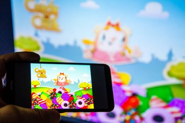 Los Angeles, Kaliforniya, ABD - 21 Şubat 2019: bir smartphone şeker ezmek Saga oyunu ile karşı büyük ekran holding eller.