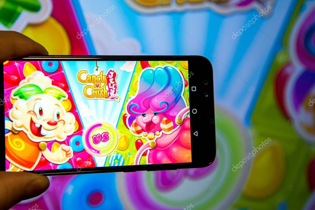Los Angeles, California, USA - 21 February 2019: Hands holding a smartphone with CANDY CRUSH SAGA game against the big screen.