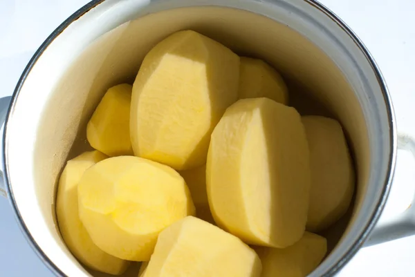 Batatas cruas descascadas em um pote em um fundo branco — Fotografia de Stock