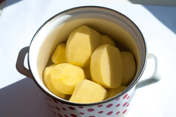 Batatas cruas descascadas em um pote em um fundo branco — Fotografia de Stock