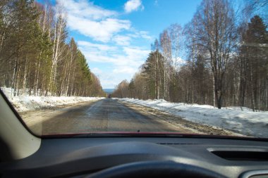 Yolun cama görünümünü. Kenarda kar. Islak asfalt yol. Mavi Gökyüzü bulutlu. Bakış açısı ile arabanın ön camdan arıyorum sürücü.