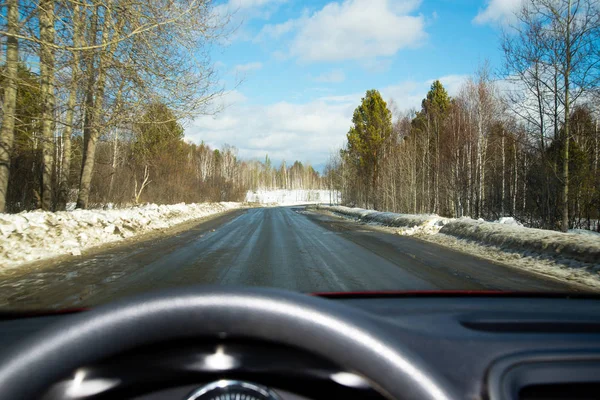 Zicht op de weg door de voorruit. Sneeuw op de zijlijn. Natte asfaltweg. Blauwe hemel met wolken. Oogpunt van de bestuurder kijken door de voorruit van de auto. — Stockfoto