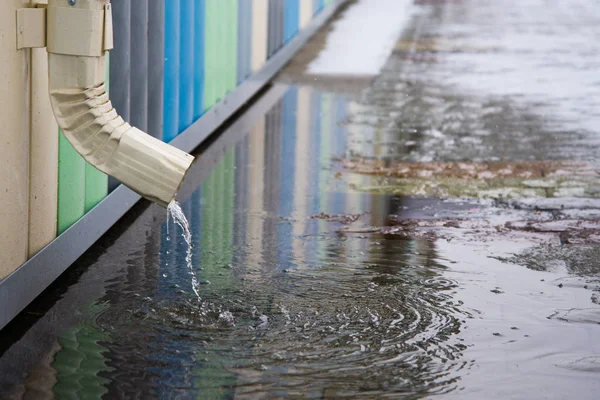 Pipa putih dengan trotoar banjir. Hujan air yang mengalir dari saluran menutup pipa Stok Gambar Bebas Royalti