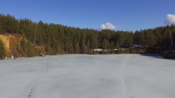 Tiro aéreo de um penhasco arborizado perto de um lago congelado em um dia ensolarado, puxar tiro — Vídeo de Stock