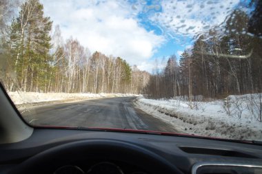Yolun cama görünümünü. Kenarda kar. Islak asfalt yol. Mavi Gökyüzü bulutlu. Bakış açısı ile arabanın ön camdan arıyorum sürücü.