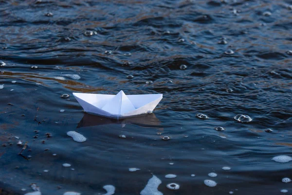 A paper boat on a turbulent stream of water struggles with the flow. Small paper boat is flowing along river.