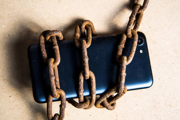 Smartphone in chains. Old rusty chains. Black smartphone.
