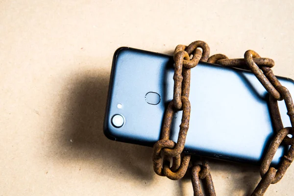 Smartphone in chains. Old rusty chains. Black smartphone.