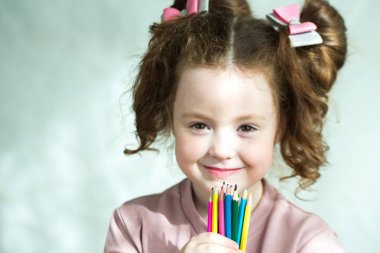 Renkli kalemler tutan ve kameraya bakan küçük kızın portresi