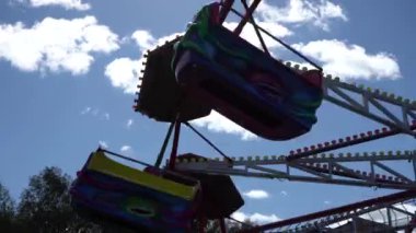 Atlıkarınca beyaz bulutların arka planına doğru hızla dönüyor. Lunaparktaki atlıkarınca, mavi gökyüzüne karşı siluet