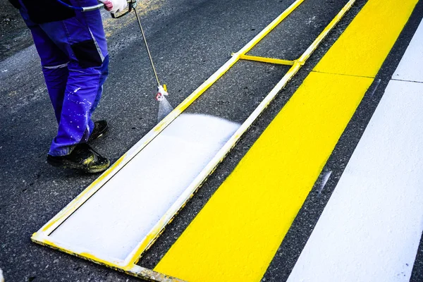 Marcación vial. Pintura de líneas de carretera. Trabajadores dibujan líneas peatonales blancas y amarillas en un cruce peatonal . — Foto de Stock