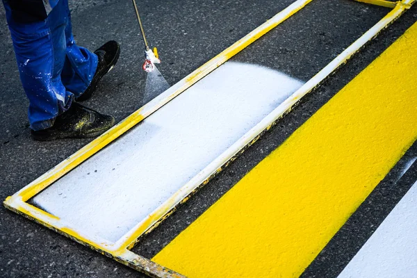 Marcación vial. Pintura de líneas de carretera. Trabajadores dibujan líneas peatonales blancas y amarillas en un cruce peatonal . — Foto de Stock