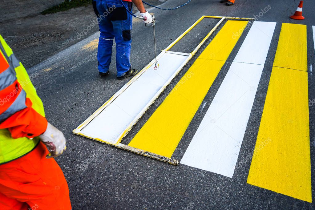 Road marking. Painting road lines. Workers draw white and yellow pedestrian lines at a pedestrian crossing.