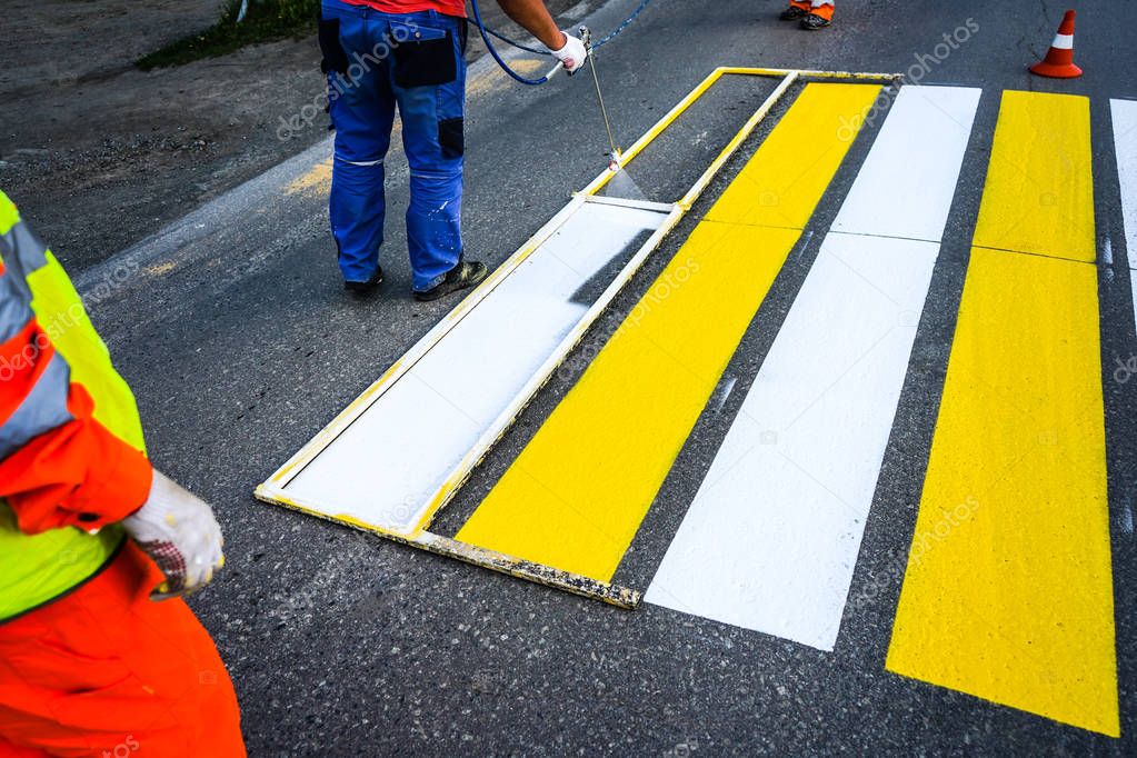 Road marking. Painting road lines. Workers draw white and yellow pedestrian lines at a pedestrian crossing.