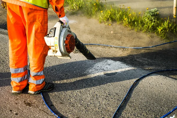 Región de Chelyabinsk, Rusia - JUNIO 2019. Camino de limpieza del trabajador de la suciedad y el polvo con la máquina de soplado para preparar el asfalto para la pintura . — Foto de Stock