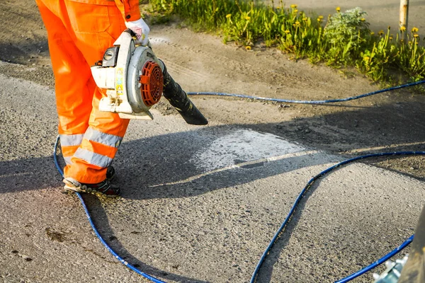 Camino de limpieza del trabajador de la suciedad y el polvo con la máquina de soplado para preparar el asfalto para la pintura . — Foto de Stock