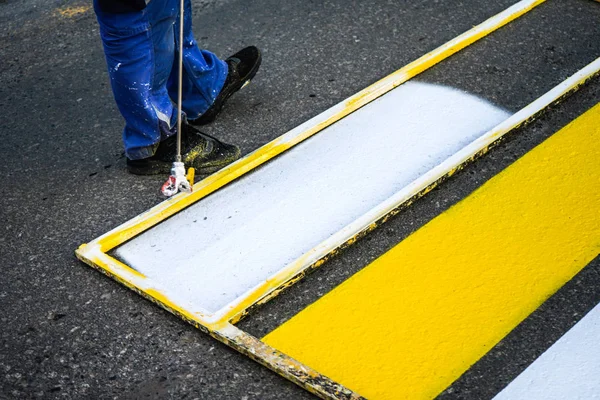 Road marking. Painting road lines. Workers draw white and yellow pedestrian lines at a pedestrian crossing.