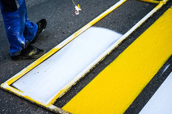 Marcación vial. Pintura de líneas de carretera. Trabajadores dibujan líneas peatonales blancas y amarillas en un cruce peatonal . — Foto de Stock