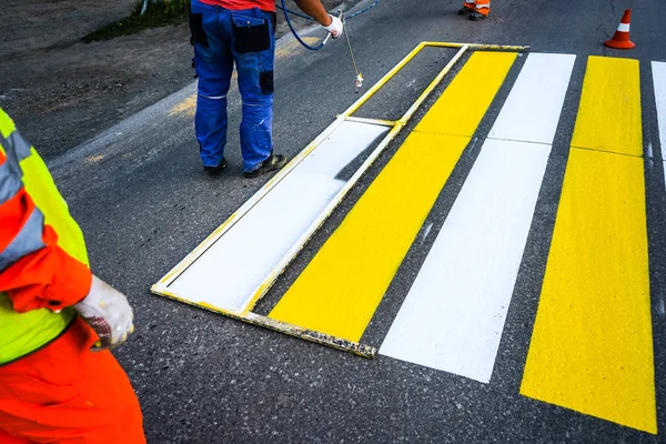 Road marking. Painting road lines. Workers draw white and yellow pedestrian lines at a pedestrian crossing.