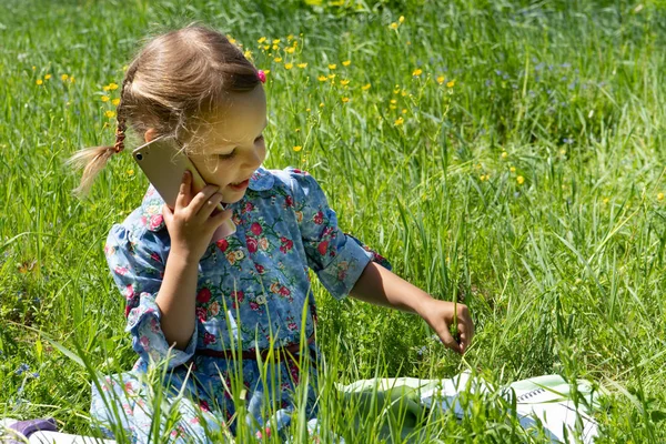Lycklig liten flicka pratar i telefon på den gröna gräsmattan. — Stockfoto