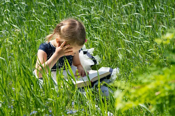 Liten flicka med en bok i trädgården. Kid är jobb en bok. En liten flicka 4-5 år gammal sitter på gräset och läser en bok. — Stockfoto