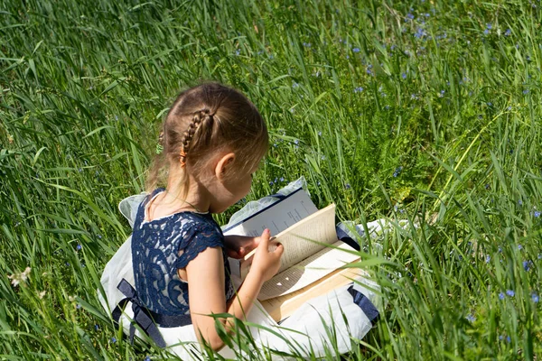 Mała dziewczynka z książką w ogrodzie. Dziecko przygotowuje książkę. Mała dziewczynka 4-5 lat siedzi na trawie i czyta książkę. — Zdjęcie stockowe