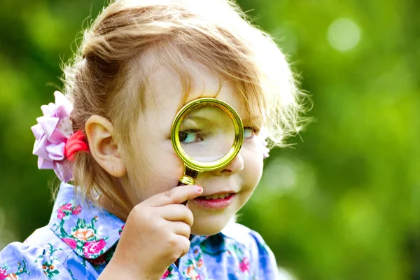 The child looks through a magnifier. Beautiful little girl looking through a magnifying glass — Stock Photo, Image