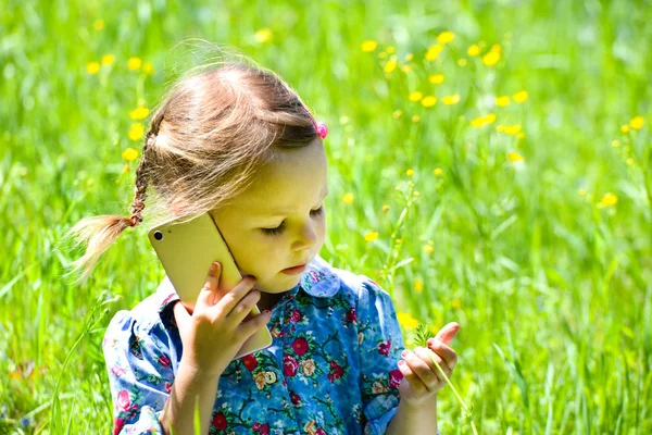 Niña feliz hablando por teléfono en el césped verde . — Foto de Stock