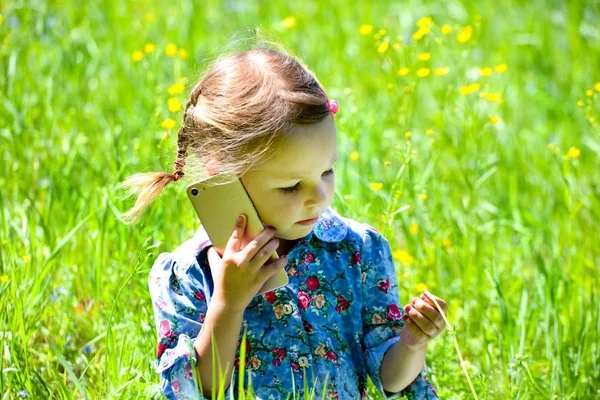 Lycklig liten flicka pratar i telefon på den gröna gräsmattan. — Stockfoto