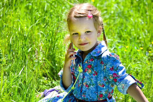 Lycklig liten flicka pratar i telefon på den gröna gräsmattan. — Stockfoto