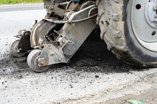 Road milling machine cuts the old asphalt. Road repair. Destruction of the road surface. The cutter cuts a layer of asphalt. Pieces of stone fly apart. Close-up