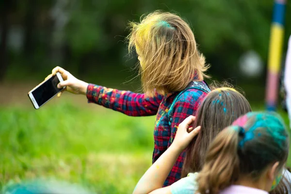 Una chica hace una selfie. Niños de diferentes nacionalidades son amigos en el festival de colores. Vacaciones en la provincia con la participación de muchas naciones, música, danza, enterta —  Fotos de Stock