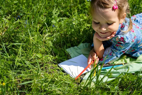 Little Happy Girl 4-5 år gammal ligger på det gröna gräset. Måla en liten rolig tjej. — Stockfoto