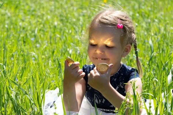 Menina segurando uma moeda criptomoeda bitcoin nas mãos. Uma criança brinca com moedas de ouro sentadas na grama . — Fotografia de Stock