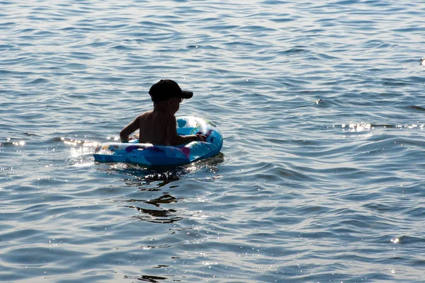 Junge schwimmt im See. um viel Sprüh- und Schaumstoff herum. Ein Kind schwimmt im See. — Stockfoto