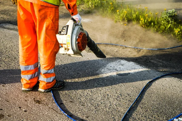 Región de Chelyabinsk, Rusia - JUNIO 2019. Camino de limpieza del trabajador de la suciedad y el polvo con la máquina de soplado para preparar el asfalto para la pintura . — Foto de Stock