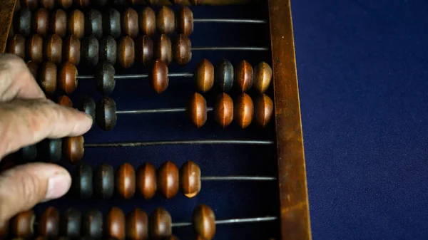 Vintage wooden abacus close up. A man s hand moves wooden knuckles on the bills. Part of the old end of the abacus on a dark blue background — Stock Photo, Image