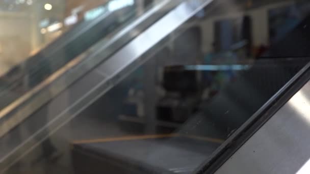 ショッピングセンターのエスカレーターステージのクローズアップ ショッピングセンターのエスカレーターの階段の動き ガラス越しに見る人のシルエットの反映 — ストック動画