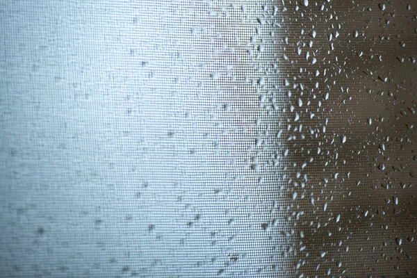 Капли дождя на москитной сетке. Москитная сетка на окне с занавесом. Горизонтальное фото, макрос . — стоковое фото