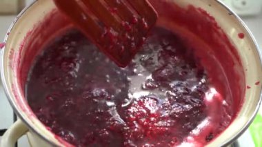 Cook ahududu reçeli ve ahşap bir spatula ile karıştırın. Bir tavada reçel karıştırın. Güneş ışığında bir tavada ahududu reçeli pişirin. Parlak renkler.