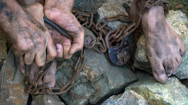 Mãos e pés de um escravo enredado em cadeias de ferro. Uma tentativa de libertar-se da escravatura. O símbolo do trabalho escravo. Mãos acorrentadas . — Fotografia de Stock