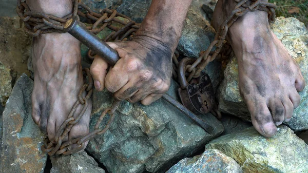 Hands and feet of a slave entangled in iron chains. An attempt to break free from slavery. The symbol of slave labor. Hands in chains. — Stock Photo, Image