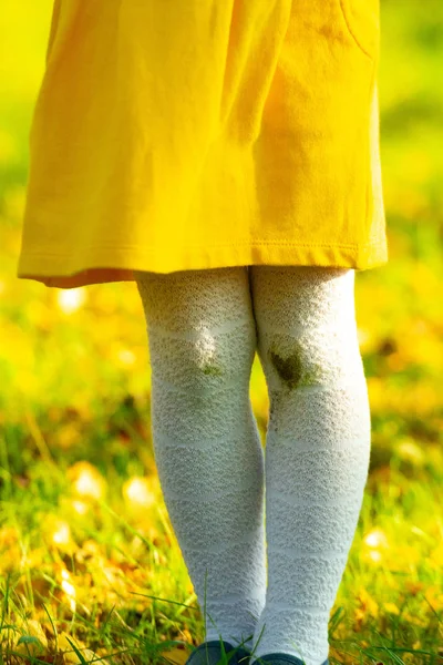 Menina em um vestido amarelo e meias brancas depois de cair no chão. Manchas de terra nos joelhos. Dia de outono. Joelhos sujos, querida . — Fotografia de Stock