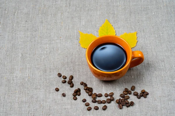 Kubek gorącej czarnej kawy królewskiej, spadł żółty liści i ziaren kawy obok tła tkaniny. Kompozycja jesień — Zdjęcie stockowe