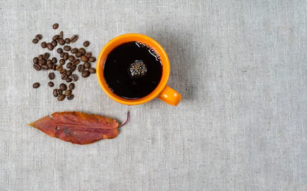 Sıcak siyah kahve bir fincan, kuru düşmüş yaprakları, bir kumaş kahve çekirdekleri. — Stok fotoğraf