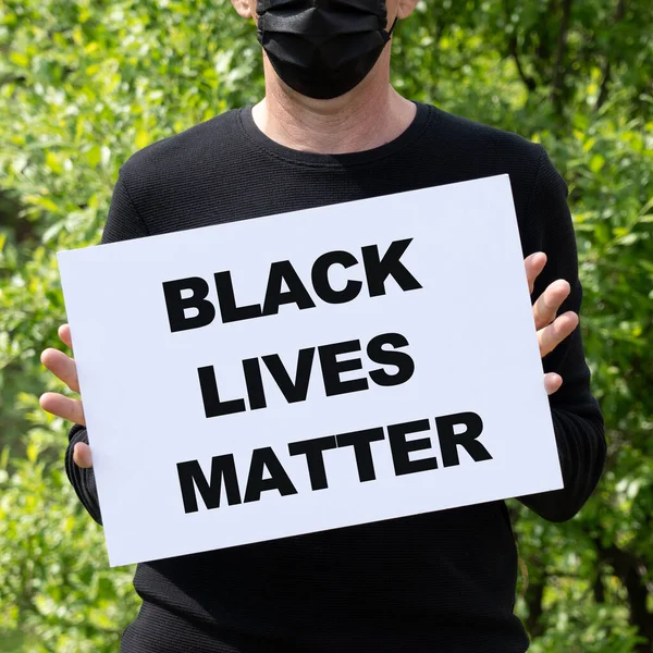 医療用ブラックマスクの男は テキストと白いバナーを保持していますBlack Lives Matter ジョージ フロイドの死をめぐって米国全土で抗議が噴出した — ストック写真