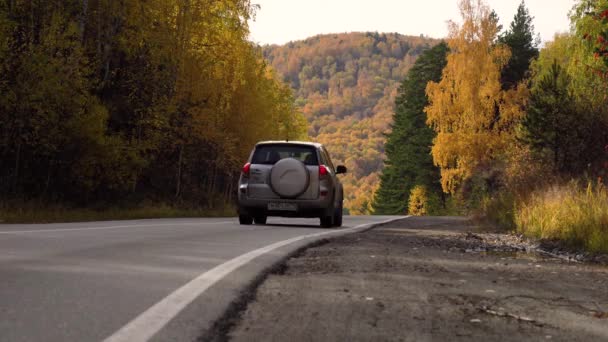 秋天坐车旅行 秋天的晴天 山地景观 树上的黄叶 空旷的郊区公路 秋天森林中的柏油路 一辆汽车在一条荒废的秋季公路上躲在地平线后面 — 图库视频影像