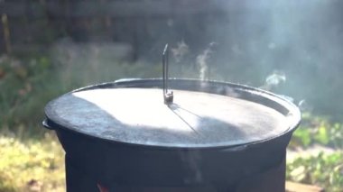 Kapağı olan büyük bir kazanda yemek pişirmek. Et haşlanır. Ateşten dumanlar yükseliyor. Kamp ateşi sırasında yemek pişiren çok büyük bir kazan. Ateşin üstünde tencerede yemek pişirmek. Kamp kavramı
